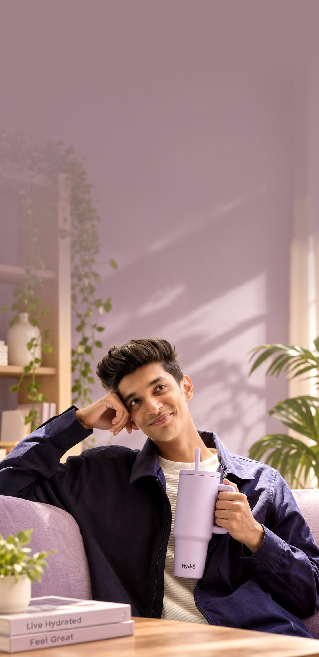 A relaxed man on a lilac sofa in a sunlit living room, holding a pastel Hydr8 tumbler
